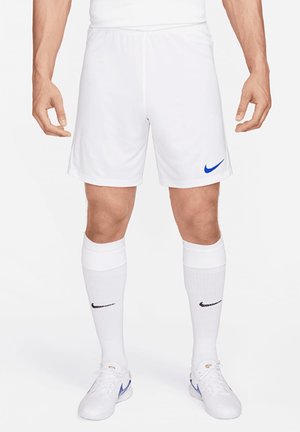 Männlich, der weiße Nike Fußballshorts, weiße Nike Socken mit schwarzem Logo und weiße Nike Turnschuhe mit blauem Swoosh trägt.