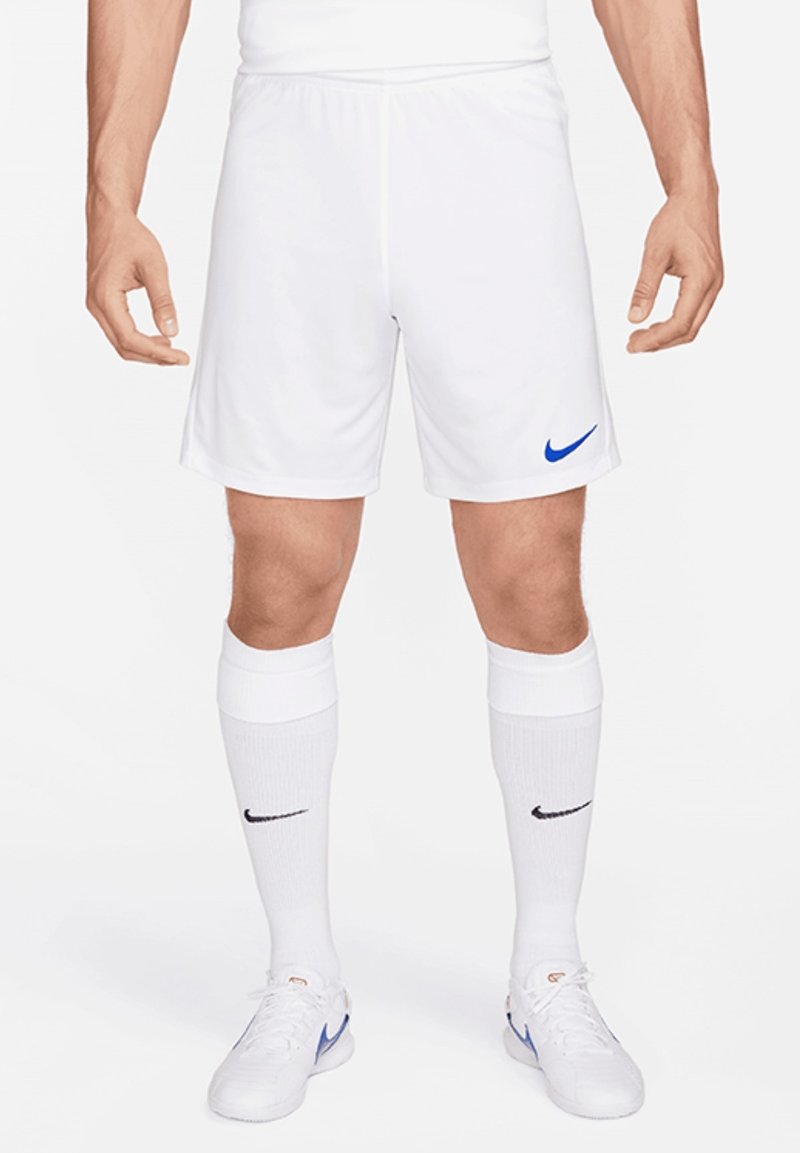Homme portant un short de football blanc Nike, des chaussettes blanches Nike avec logo noir, et des baskets blanches Nike avec le swoosh bleu.