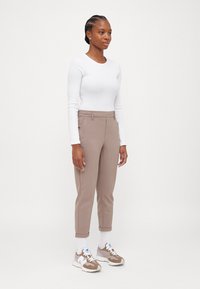 Lätt vit långärmad topp parat med skräddarsydda ljusbruna byxor med uppvikt nederkant och sidofickor. Avslutad med neutrala sneakers.