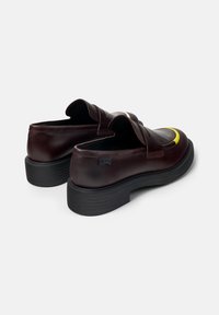 Bordeaux leren schoenen met een laag profiel, ronde neus, zwarte rubberen zool en gele accenten aan de voorkant, met een instapontwerp.
