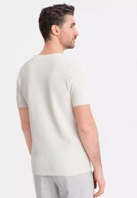 Suéter de manga corta, color beige claro, textura de punto, cuello y puños acanalados, forma ajustada, diseño liso sin acentos visibles.