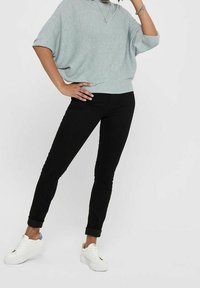 Jasnoszary, oversize sweter z krótkimi rękawami, zestawiony z dopasowanymi czarnymi dżinsami i białymi sneakersami. Strój cechuje się luźnym, nowoczesnym stylem.