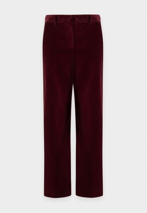 Femme portant un polo à manches longues rayé bleu marine et blanc et un pantalon large taille haute rouge foncé, debout devant un fond uni.