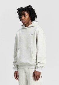 Ljusgrå hoodie gjord av mjukt tyg, med en kenguruficka, ribbade manschetter och ordet "ETERNITY" tryckt på bröstet.