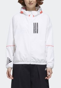 Hvid vindjakke med sort tre-stribedesign og branding. Den har en hætte, elastiske manchetter og en diskret pink detalje på ærmerne.