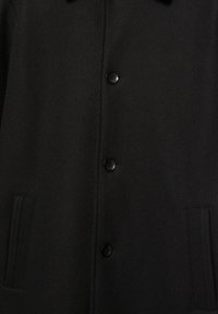 Zwarte wollen jas met een knopenrij aan de voorkant, twee zijzakken en een gladde textuur. Eenvoudig ontwerp met een gestructureerde kraag en strakke lijnen.