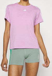 Camiseta atlética rosa de manga corta con logo blanco en el pecho, combinada con pantalones cortos ajustados verdes con detalles laterales y logo.