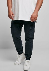 Mörkblå cargobyxor med flera sidofickor, avsmalnande anklar och elastiska muddar, ihop med vita sneakers och en enkel vit t-shirt.