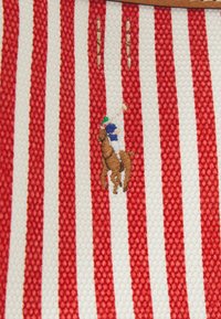 Červenobíle pruhovaná tkanina zdobená vyšitou postavou jezdce na koni s propracovanými detaily na jezdcově oblečení a koni.