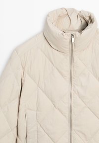 Beżowa pikowana kurtka z wysokim kołnierzem, przednim zamkiem błyskawicznym i bocznymi kieszeniami. Wykonana z gładkiego, lekkiego materiału o subtelnym połysku.