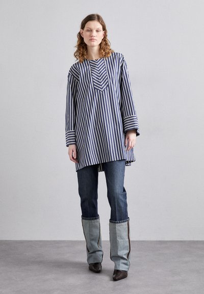 Tunique rayée bleu marine et blanc avec un décolleté en V et des manches longues, associée à un jean en denim bleu et des accents en denim bleu clair évasés.