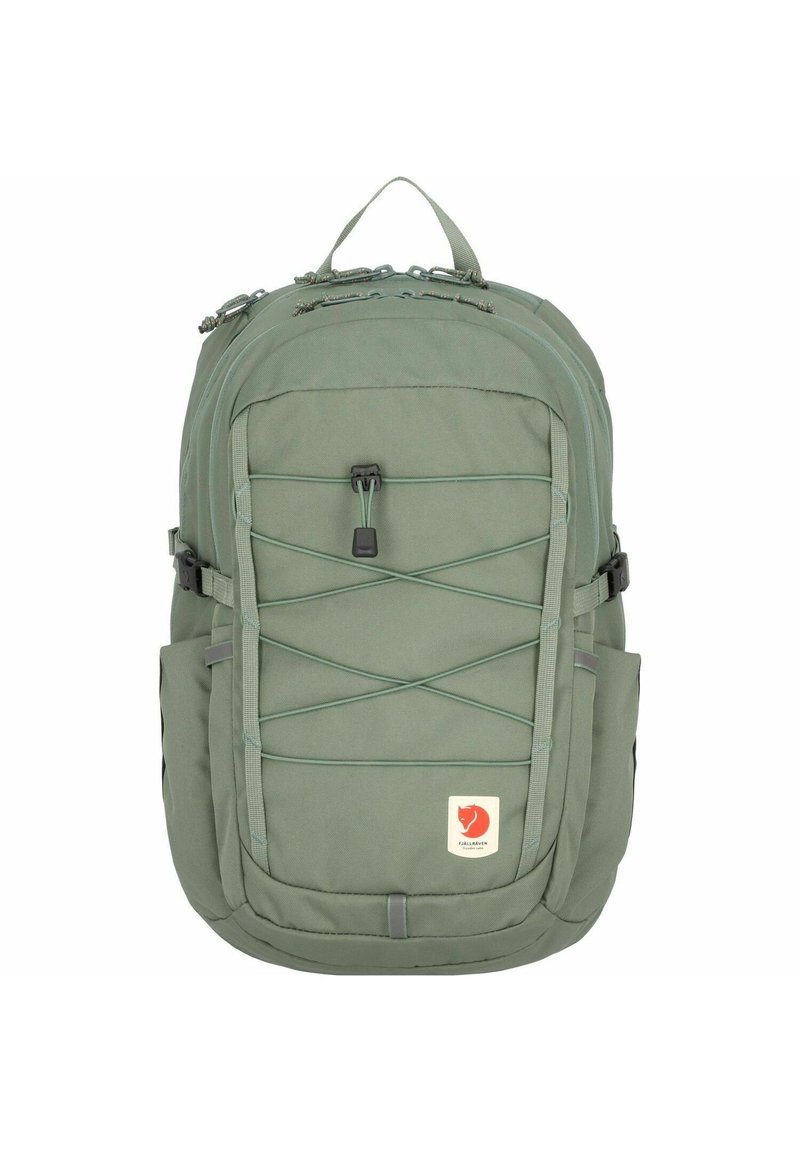 Grønn stoffryggsekk med et robust design, har mesh sidelommer, frontbungee-kord og en logopatch nederst.