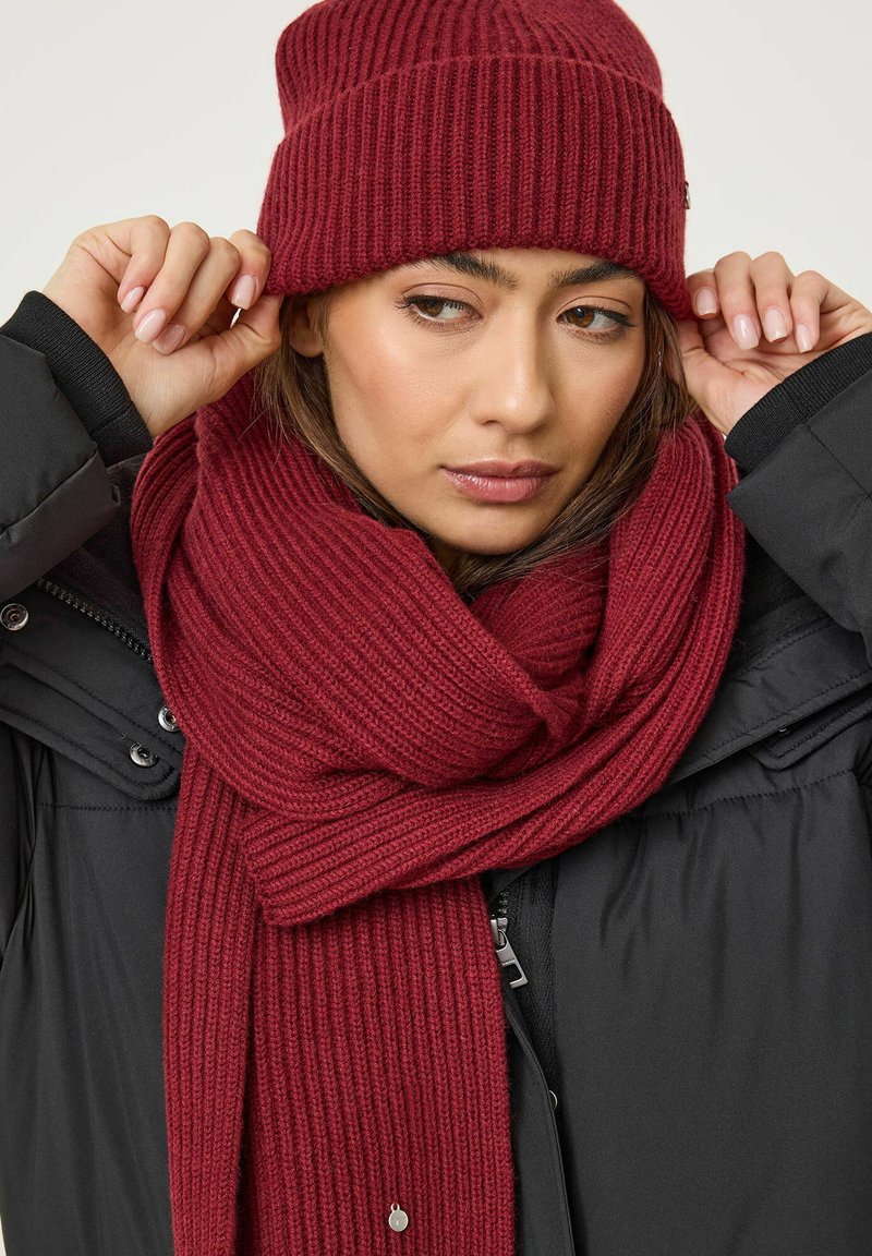 Ribbelige bordeaux gebreide beanie en sjaal combinatie, met een zachte textuur, gedragen over een zwarte pufferjack, ontworpen voor warmte.