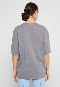 Camiseta gris de gran tamaño con mangas cortas, que presenta una textura suave y un escote redondo. Vista trasera muestra un patrón sutilmente desvaído y sin logotipos visibles.