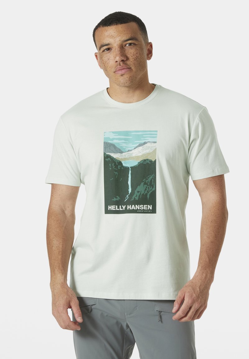 Světle zelené bavlněné tričko s centrálním grafickým motivem hor a vodopádu, s textem "HELLY HANSEN" na spodní části. Krátké rukávy.