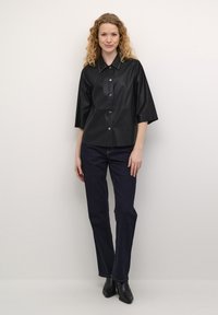 Melnās mākslīgās ādas blūze ar apkakli, zīmējumu ar uzlīmi un pusgarām piedurknēm, apvienota ar tumšām džinsām un melnām potīšu zābakiem.