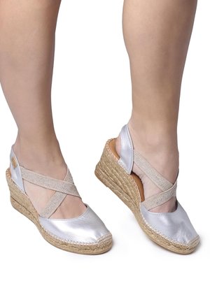 Silver metallic wedge sandals with cross-strap design, woven jute heel, and a smooth toe cap. Flat heel and open-back style.