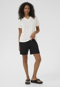 T-shirt blanc à col en V assorti à un short noir. Le t-shirt a des manches courtes et une coupe décontractée ; le short est de longueur genou, avec une texture lisse.