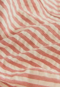 Un tissu à rayures rouges et crème présente un tissage texturé avec des lignes horizontales alternées. Le matériau semble doux et léger.