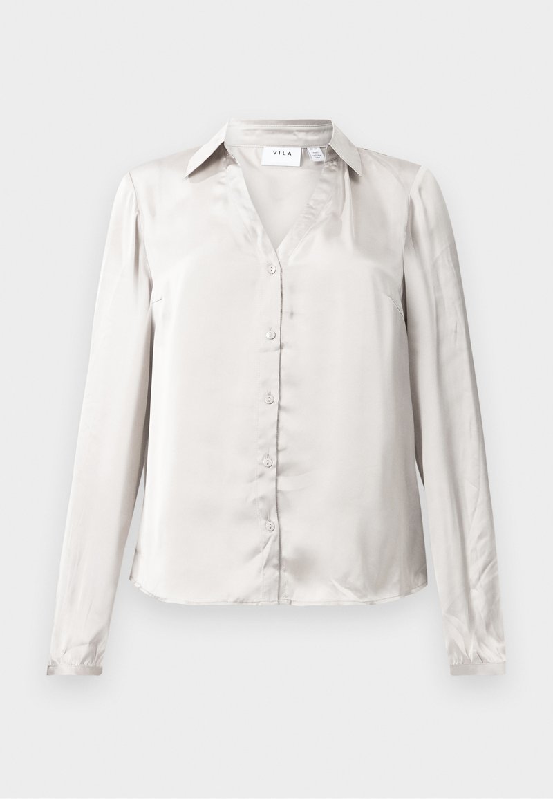 Blouse beige clair en satin à manches longues, avec un col, légèrement cintrée et texture lisse et soyeuse.