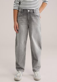 Heledashallased kõrge vöökohaga lahtise istuvusega teksapüksid, mis on tuhmunud värvitooni ja esitaskutega, nööpidega kinnitatavad, mille juurde on valitud valged ja hõbedased tossud.