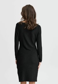 Schwarzes, langärmliges Kleid, knielang, aus strukturiertem Stoff mit leichtem Schimmer. Schlichtes Design, Rundhalsausschnitt und figurbetonte Silhouette.