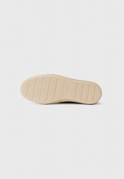 Beige rubber sole of a casual shoe with horizontal grooves and textured grip, lying flat on a white surface.