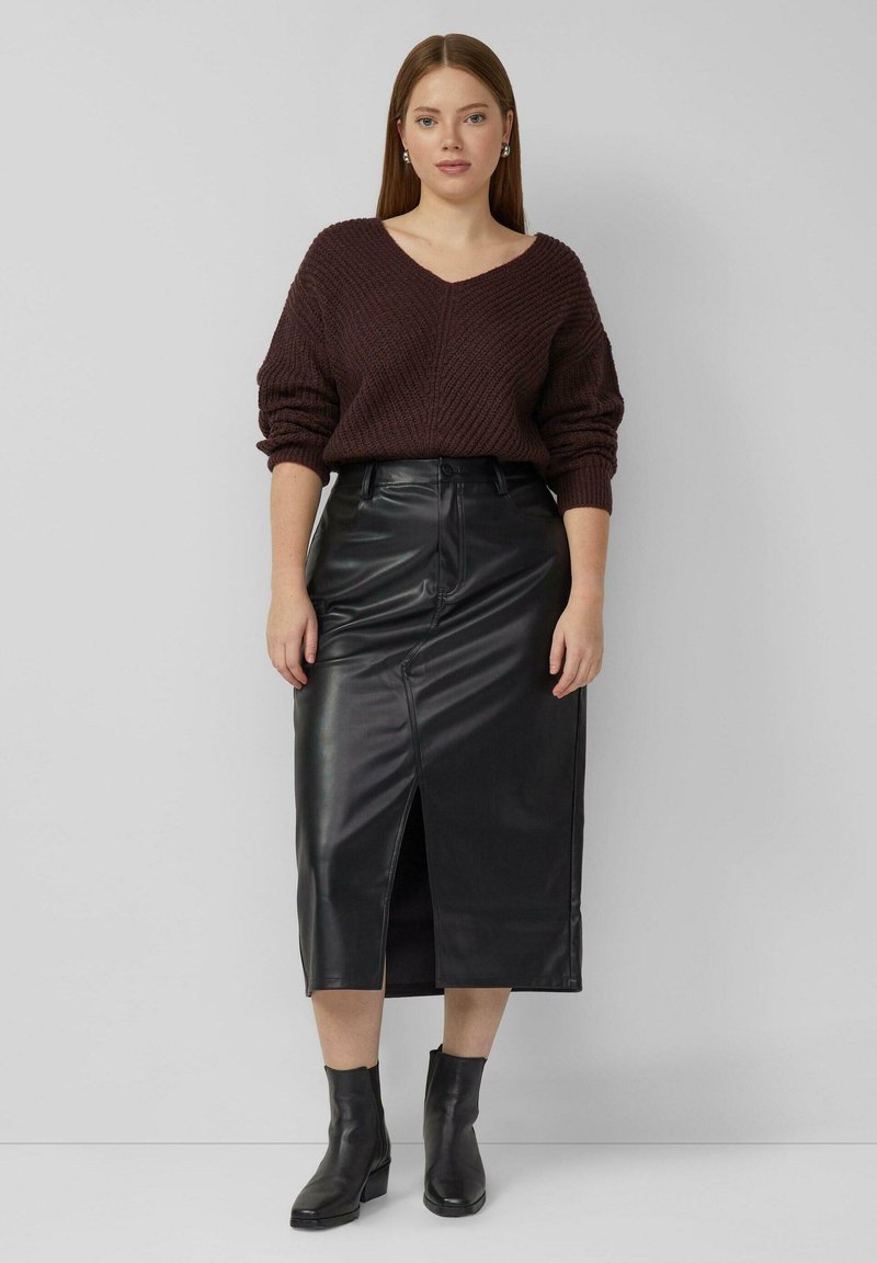 Pull en tricot bordeaux à col en V, associé à une jupe midi en cuir noir avec une fente avant, et des bottines noires.