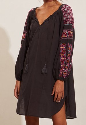 Czarna luźna sukienka z kolorowymi, kwiatowymi i geometrycznymi haftowanymi długimi rękawami oraz dekoltem w serek z frędzlami do wiązania.