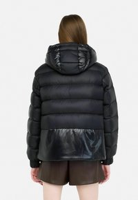 Giubbotto puffer nero con una sezione inferiore lucida, cappuccio e texture trapuntata. Presenta polsini elasticizzati e un design leggermente accorciato.