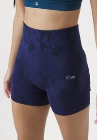 Høyt midjebåndet trening-shorts i mørk lilla med et subtilt mønster, med en tett passform og ICIW-logo på siden. Glatt tekstur.