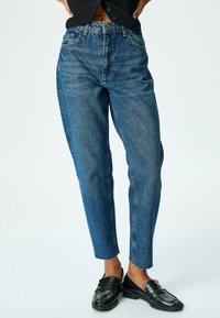 Jeans de mezclilla azul de cintura alta con un corte recto, textura deslavada y dobladillo sin terminar. Combinados con mocasines negros.