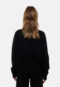 Pull noir surdimensionné avec des manches longues, des poignets et un ourlet côtelés. Texture douce, design uni, stylé de dos avec les cheveux visibles.