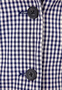 Tessuto a quadri navy e bianco con una consistenza liscia, caratterizzato da un grande bottone nero e dettagli di cucitura ben visibili.