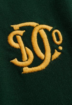 Geel gestileerde "S" en "O²" borduursel op een donker groene, gestructureerde stoffen achtergrond, close-up weergave.