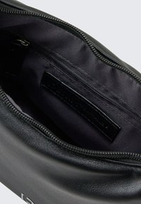Schwarze Leder-Clutch mit Reißverschluss, ausgestattet mit einem dunklen Innenfutter und einer inneren Reißverschlusstasche. Schlichte, runde Form mit minimalem Zubehör.