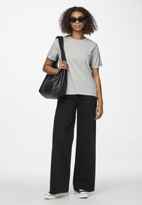 Grå bomulls T-skjorte med korte ermer, kombinert med vide svarte jeans. Modellen bærer en svart lær toteveske og har på seg mørke solbriller.