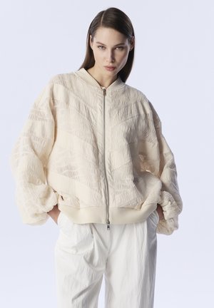 Blouson bomber couleur crème avec un design texturé, doté d'une fermeture éclair à l'avant, de manches ballons et de poignets et d'un ourlet côtelés.