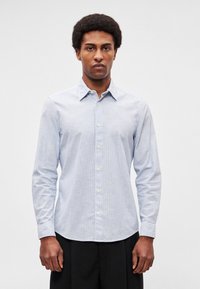 Ανοιχτό μπλε πουκάμισο με κουμπιά, κατασκευασμένο από υφή ύφασμα, με μυτερό γιακά, μακριά μανίκια και διακριτικές κάθετες ρίγες.