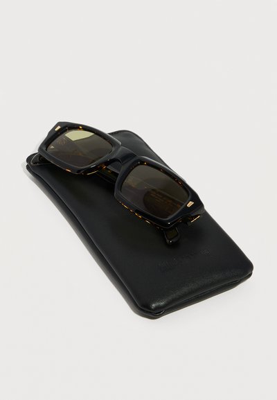 Μαύρα ορθογώνια γυαλιά ηλίου με άκρες από χελώνα, τοποθετημένα πάνω σε μαύρη μαλακή δερμάτινη θήκη, σε ανοιχτό φόντο.