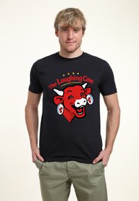Černé bavlněné tričko s grafickým motivem červené krávy s náušnicemi, textem "Smějící se kráva" a pěti zlatými hvězdami nad designem.