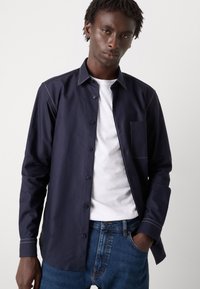 Navy button-up shirt made of soft fabric, featuring a chest pocket, contrasting white stitching, and a relaxed fit, paired with denim jeans.