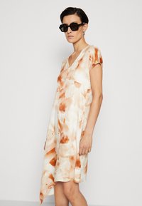 Rochie ușoară cu un model abstract în nuanțe de crem și portocaliu, având mâneci scurte și o linie de tiv asimetrică.