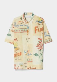Camisa de manga corta con cuello, fabricada en un tejido beige claro con estampados coloridos de estilo vintage, que incluyen flores y texto relacionado con Florida.
