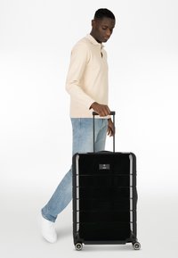 Black hard-shell suitcase with a glossy finish, extending handle, and four wheels. Features a top handle and embossed brand logo.