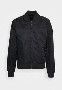 Giacca bomber nera realizzata in tessuto liscio, con chiusura a zip frontale, polsini e fondo a coste, e delicata ricamo del logo sul petto.