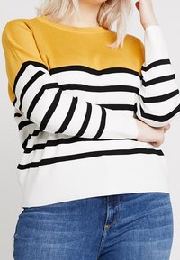 Pull tricoté avec des rayures horizontales noires et blanches et une partie supérieure jaune moutarde. Col rond et coupe décontractée.