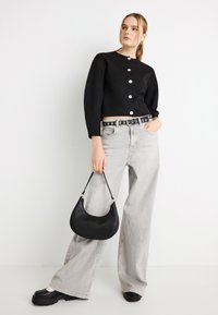 Μαύρο cropped πουλόβερ με στρογγυλή λαιμόκοψη και κουμπιά μπροστά, συνδυασμένο με ψηλόμεσο ανοιχτογκρι τζιν με φαρδιά παντελόνια και μαύρη τσάντα.