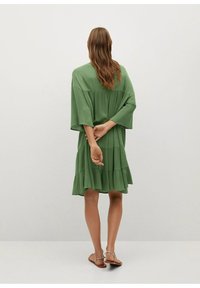 Abito verde a maniche corte con gonna a strati, caratterizzato da una vestibilità comoda e un tessuto testurizzato. La parte posteriore presenta un design semplice, che accentua il movimento.