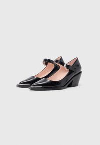 Black patent leather Mary Jane shoes with a pointed toe, ankle strap, and a low wedge heel. Smooth texture and minimal hardware accents.